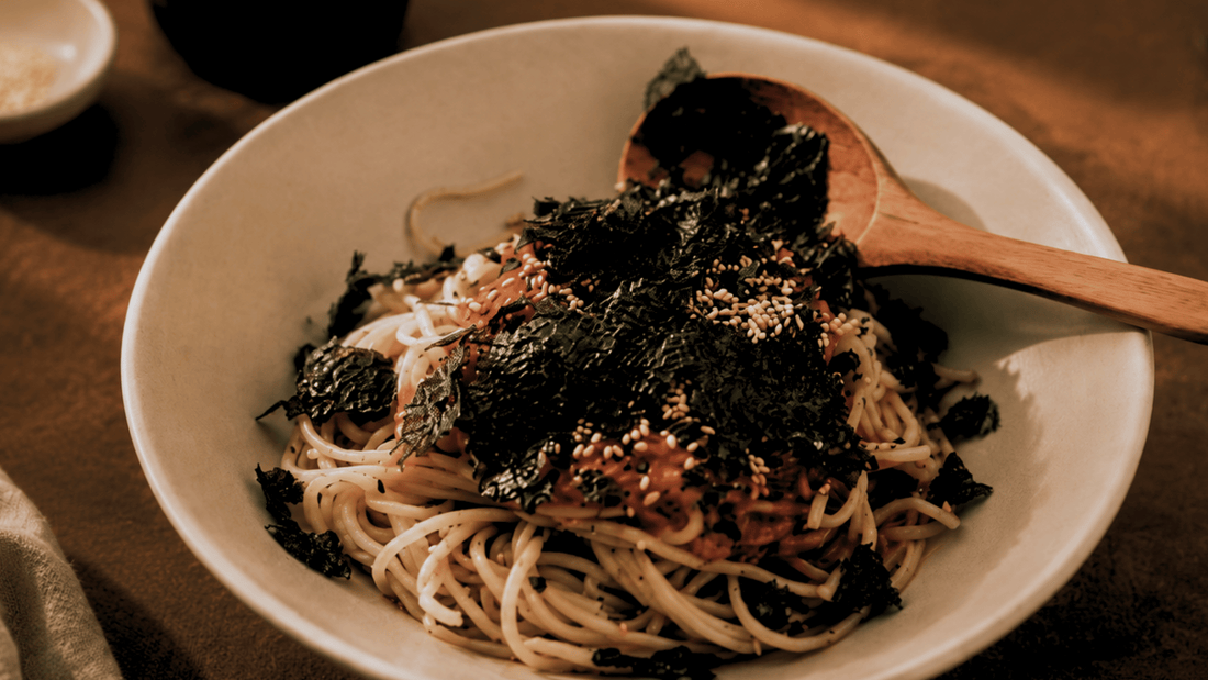 Viral Korean Spicy Tomato Bibim Guksu Cold Noodle bowl with seaweed topping and a spoon on the side of the bowl. 