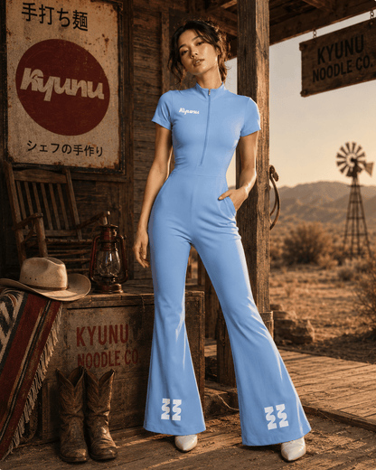 Model in the light blue Kyunu jumpsuit on a desert porch beside Kyunu Noodle Co. signage