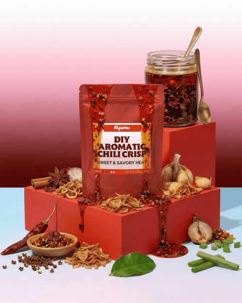 Kyunu DIY Aromatic Chili Crisp pouch beside a jar of chili crisp, garlic, shallots and dried chilies