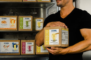 Muscular Man holding a box of KYUNU Rulebreaker Protein Noods, Original Flavor in front of KYUNU Rulebreaker Protein Noodles Boxes in Freezer