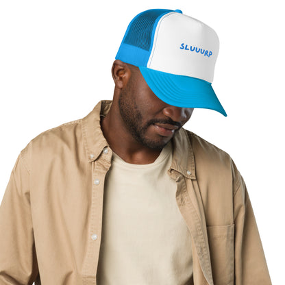 Person in a tan overshirt wearing the blue Sluuurp trucker hat, angled side view
